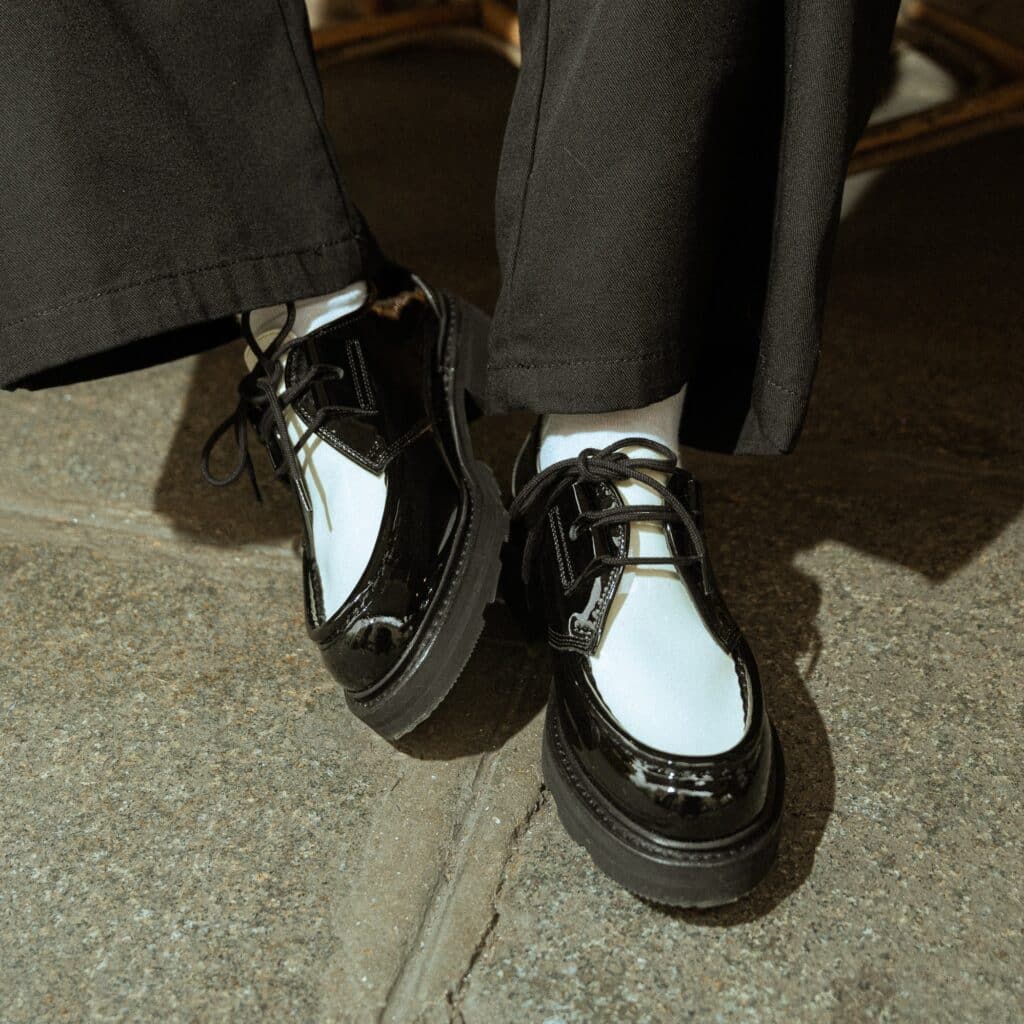 Derbies femme Paraboot Beaubourg bicolores en cuir vernis noir et cuir lisse crème portées avec des chaussettes blanches