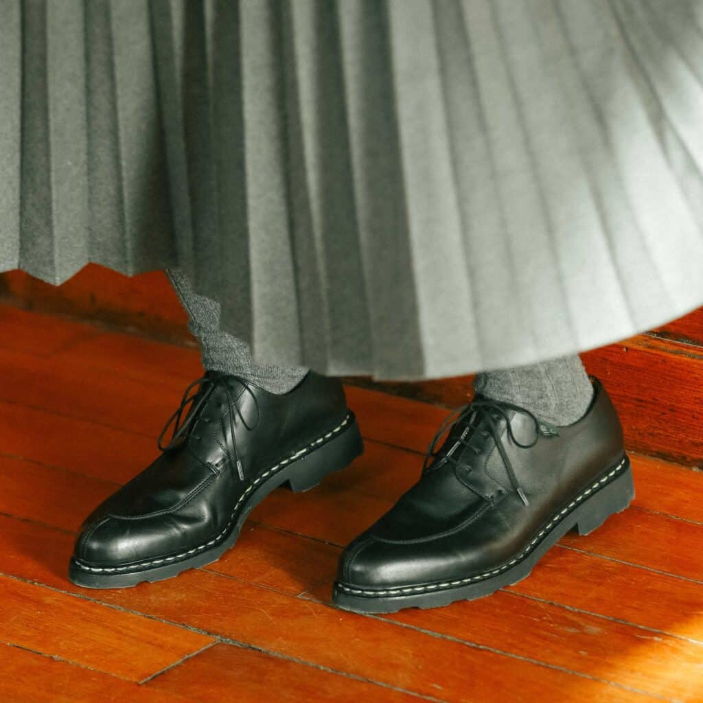 Chaussures Paraboot Veley en cuir lisse noir à bout chasse, portées avec une jupe plissée grise et des chaussettes en laine.