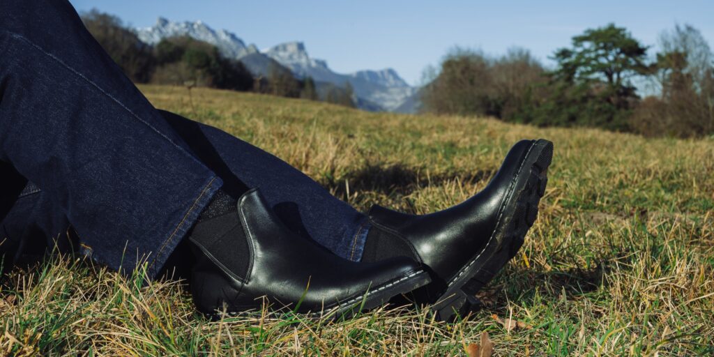 Black Paraboot women's Chelsea boots model Valdaine worn in a field with mountains in the distance.