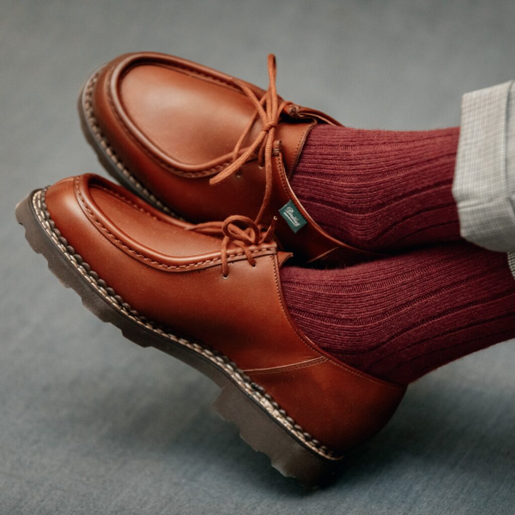 Chaussures Paraboot Michael en cuir lisse marron avec cousu norvégien apparent, portées avec des chaussettes bordeaux côtelées et un pantalon gris à carreaux.