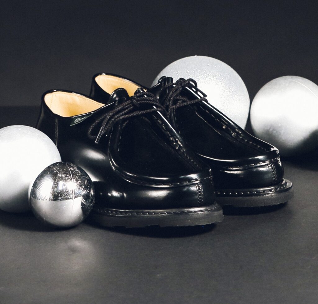 Chaussures Paraboot Michael en cuir vernis noir entourées de boules de Noël argentées sur fond sombre.