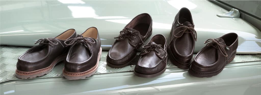 Chaussures Paraboot iconiques en cuir grainé marron posées sur le capot et le moteur d'une voiture de collection.