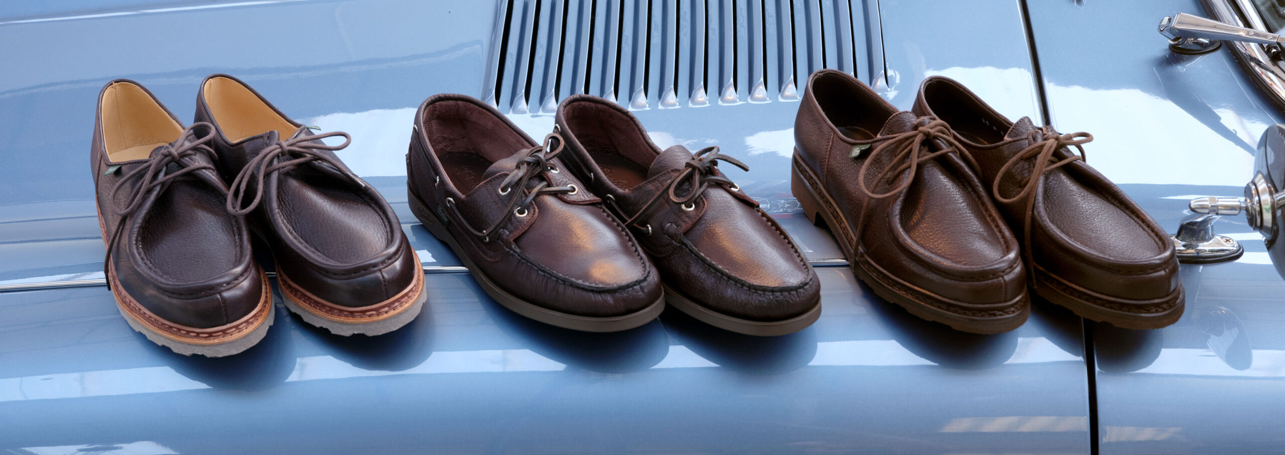 Iconic Paraboot shoes in brown grained leather set on the hood and engine of a vintage car.