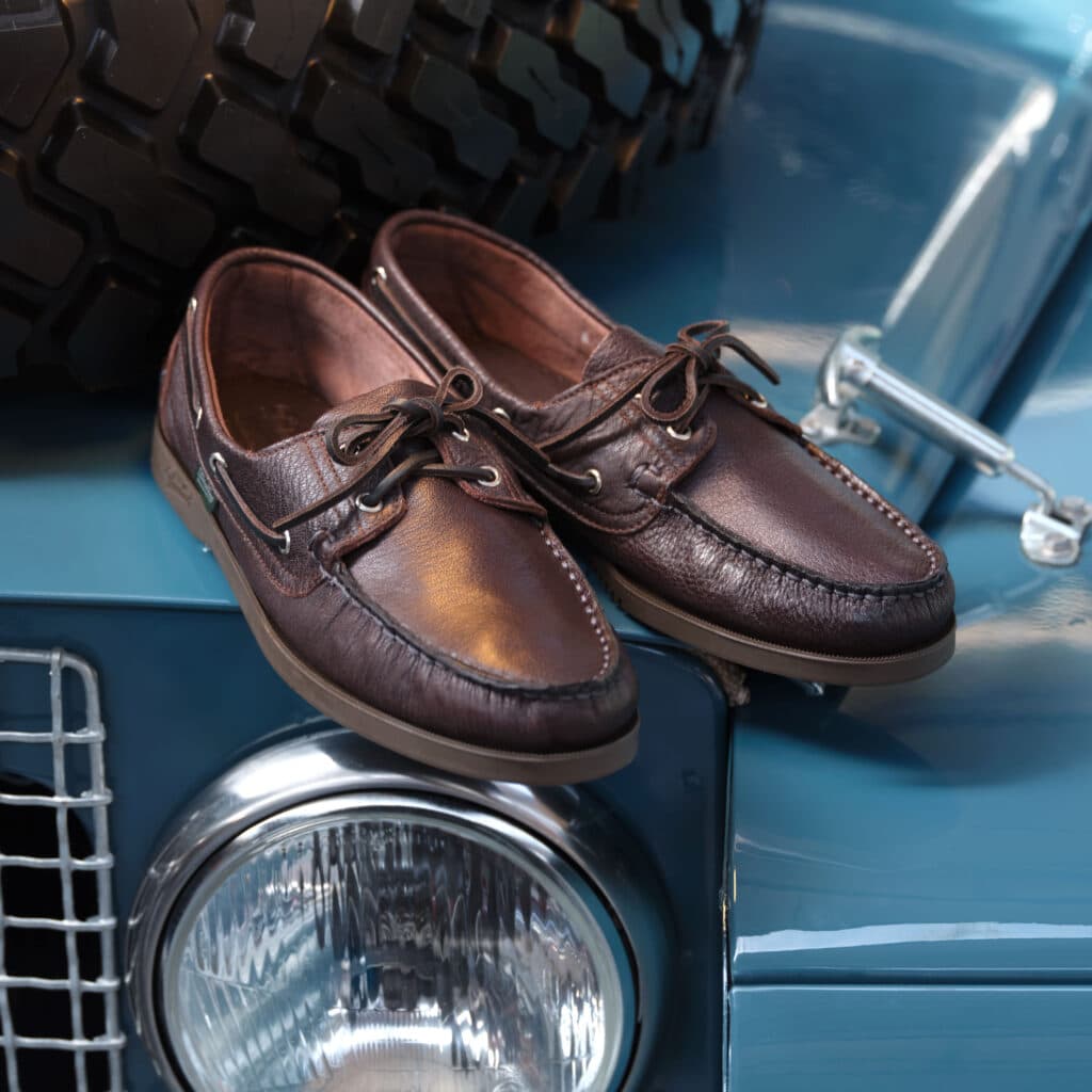Chaussures Barth iconiques en cuir cerf marron posées sur le capot d'une voiture de collection.