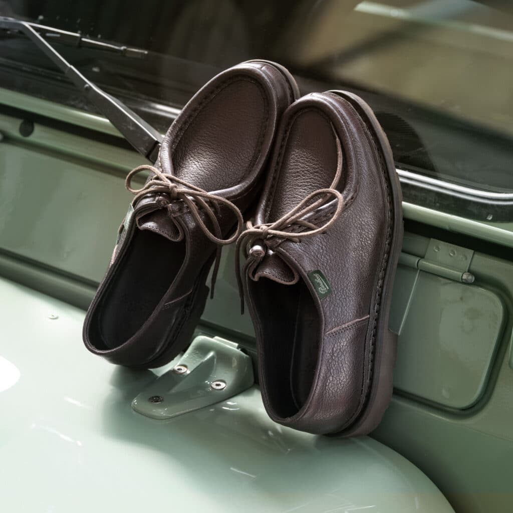 Chaussures Michael iconiques en cuir cerf marron posées sur le pare-brise d'une voiture de collection.