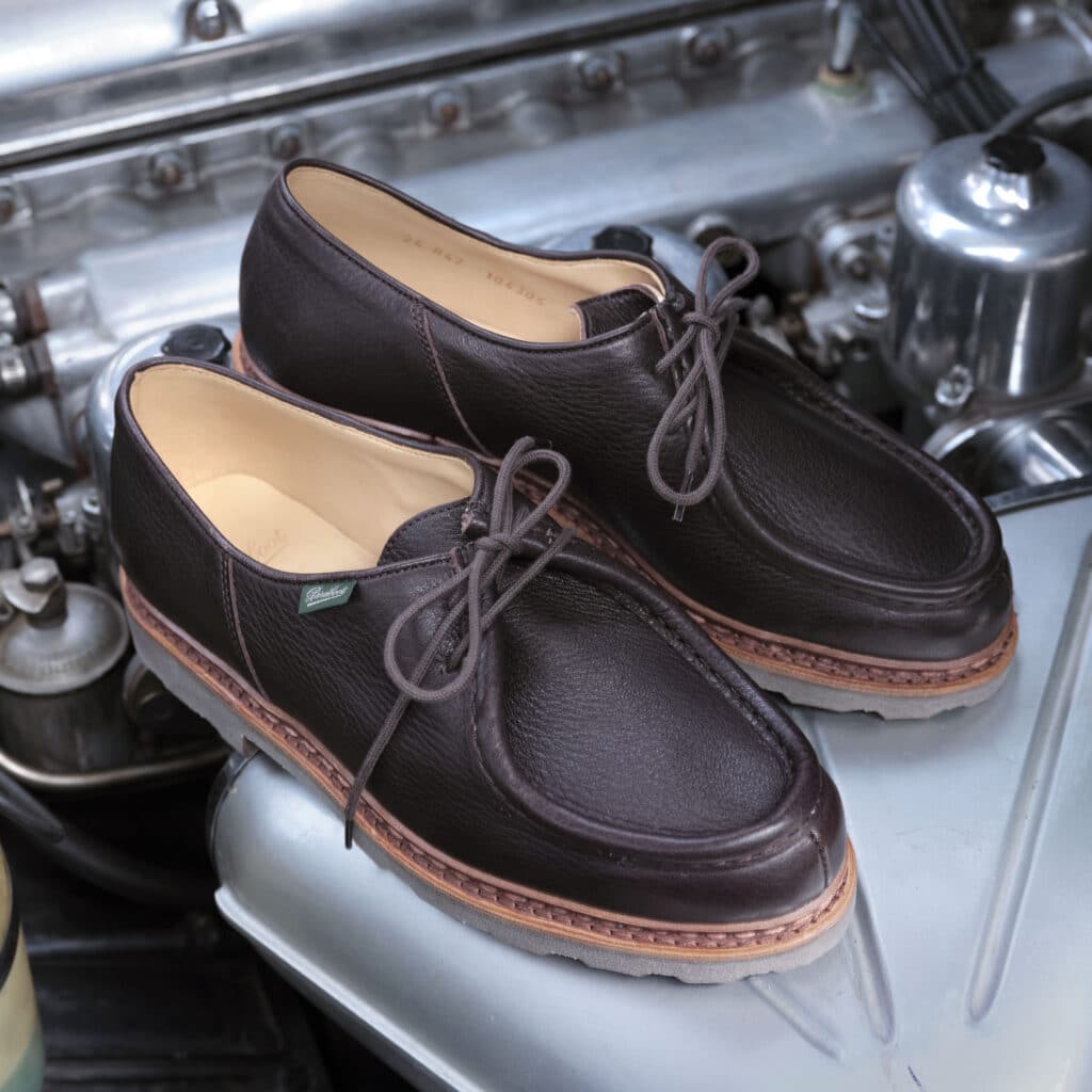 Chaussures Paraboot iconiques en cuir grainé marron posées sur le moteur d'une voiture de collection.