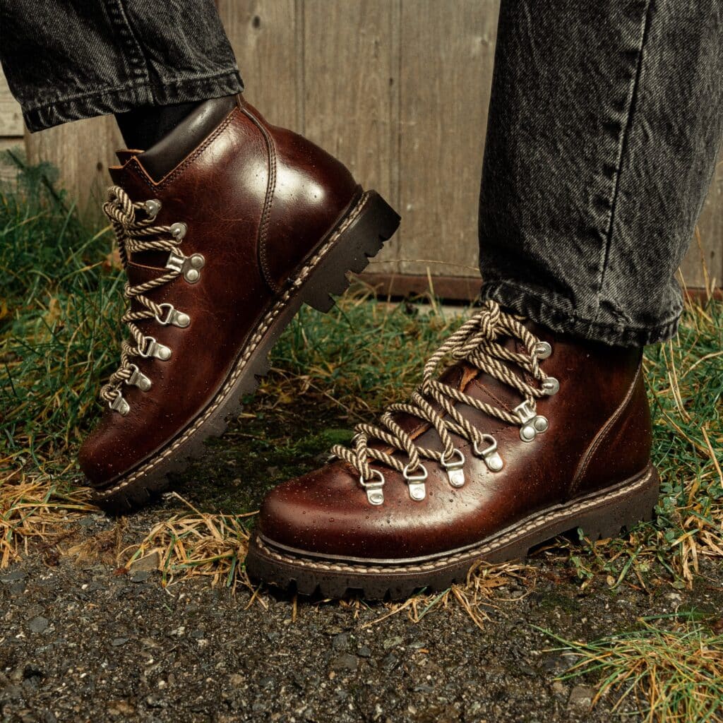 Gros plan de bottines de ville femme Paraboot Avoriaz en cuir lisse écorce marron foncé avec semelle commando et laçage montagne, portées sur gravier avec un jean noir.