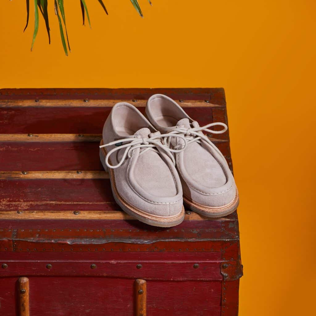 Paire de chaussures à lacets Mirabelle de Paraboot en velours grès posée sur une malle vintage rouge sur fond orange.