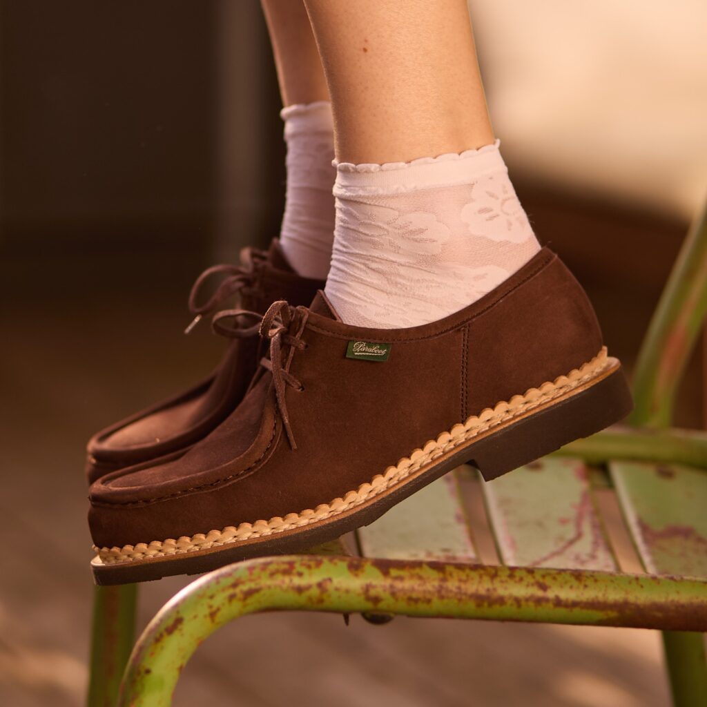 Zoom sur les chaussures à lacets Mirabelle de Paraboot en nubuck taurillon chocolat, portées sur un escalier en béton avec un pantalon à rayures.