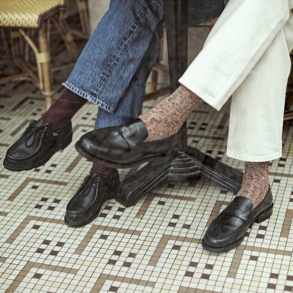 Vue d'ensemble de deux personnes en terrasse, portant des chaussures Paraboot : le modèle Michael lisse noir et le mocassin Adonis lisse noir avec chaussettes texturées.