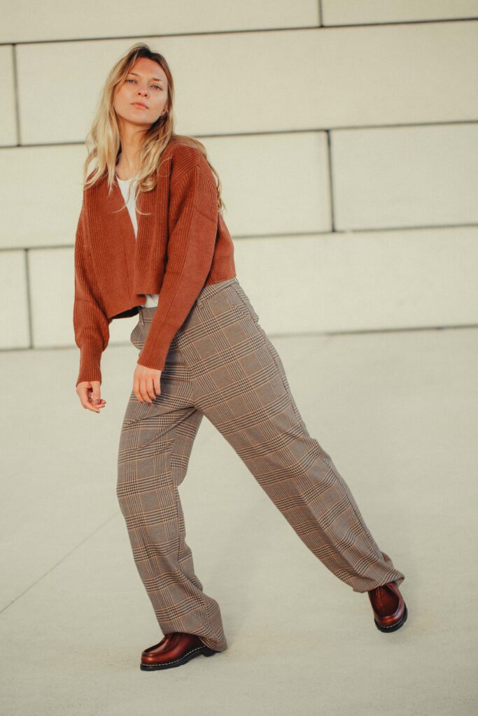 Silhouette de femme portant les chaussures Paraboot Michael en cuir marron, associées à un pantalon à carreaux et un gilet rouille pour un look automnal.