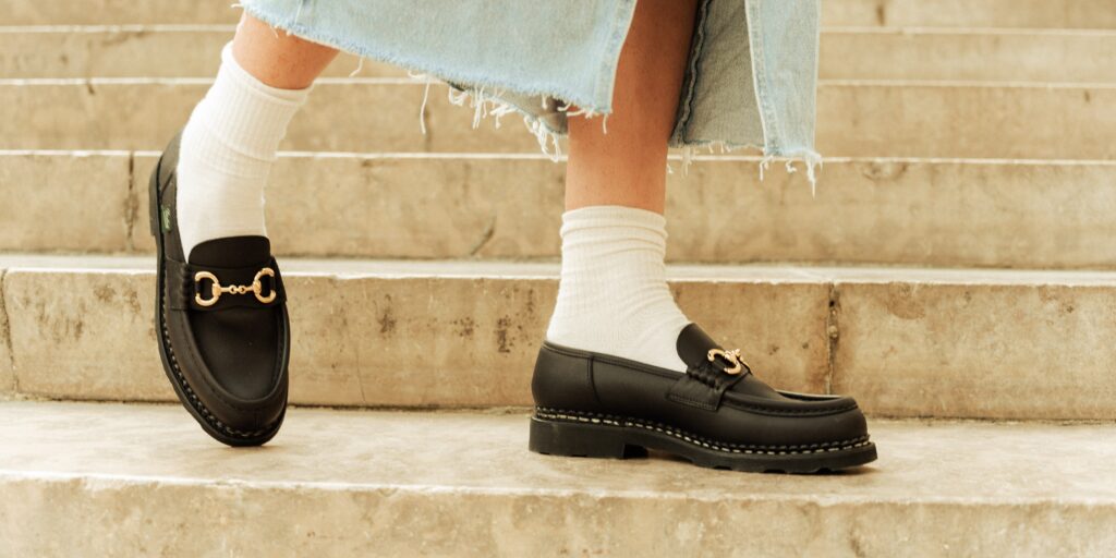 Orsayti de Paraboot en cuir lisse noir avec mors doré, présentés avec une jupe en jean déchiré.