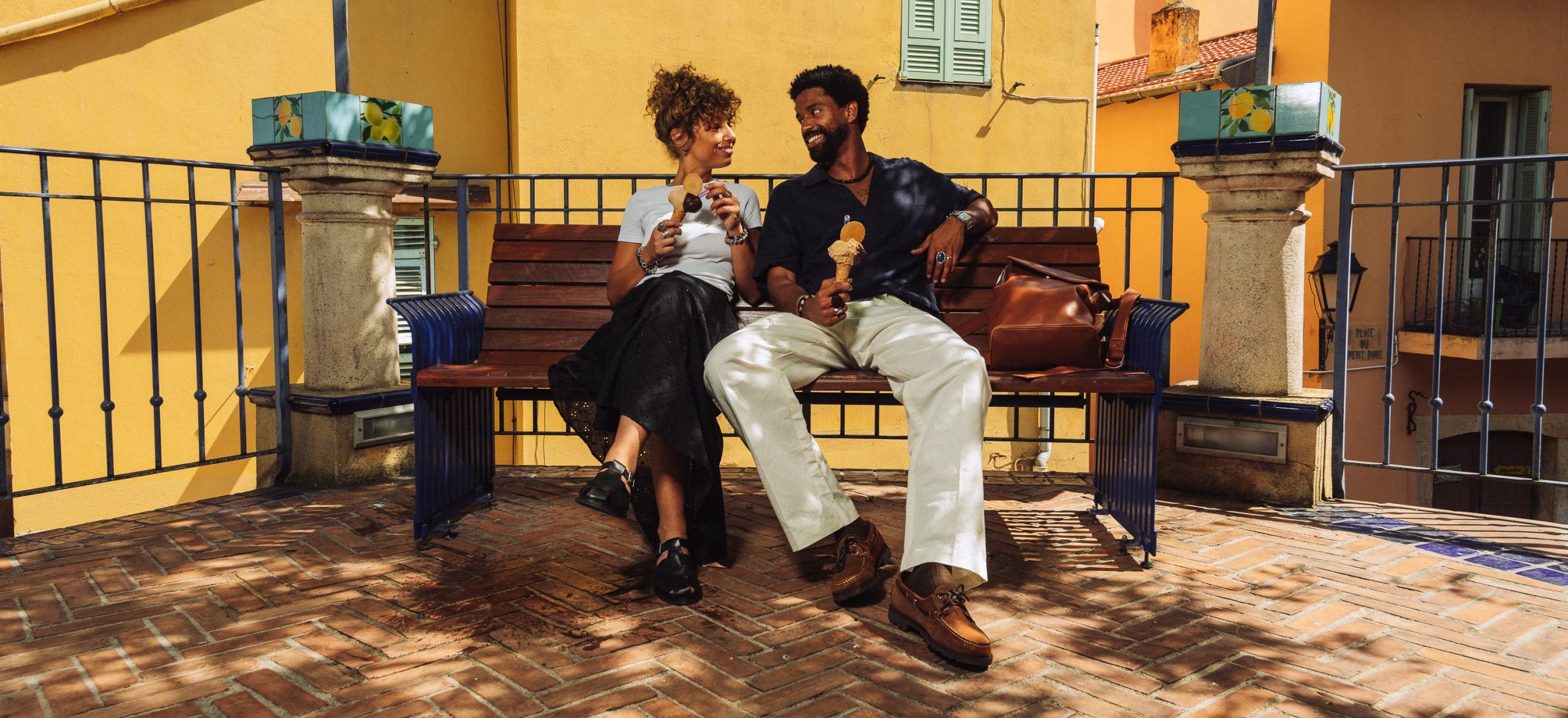 Couple dégustant une glace sur un banc à Menton, portant des sandales et chaussures bateau d'été Paraboot.