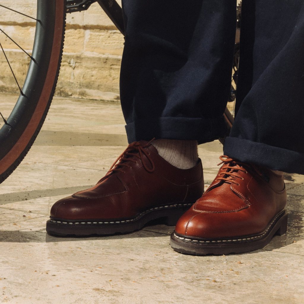 Paire de derbies pour homme Paraboot Avignon en cuir lisse marron portée à côté d'une roue de vélo.
