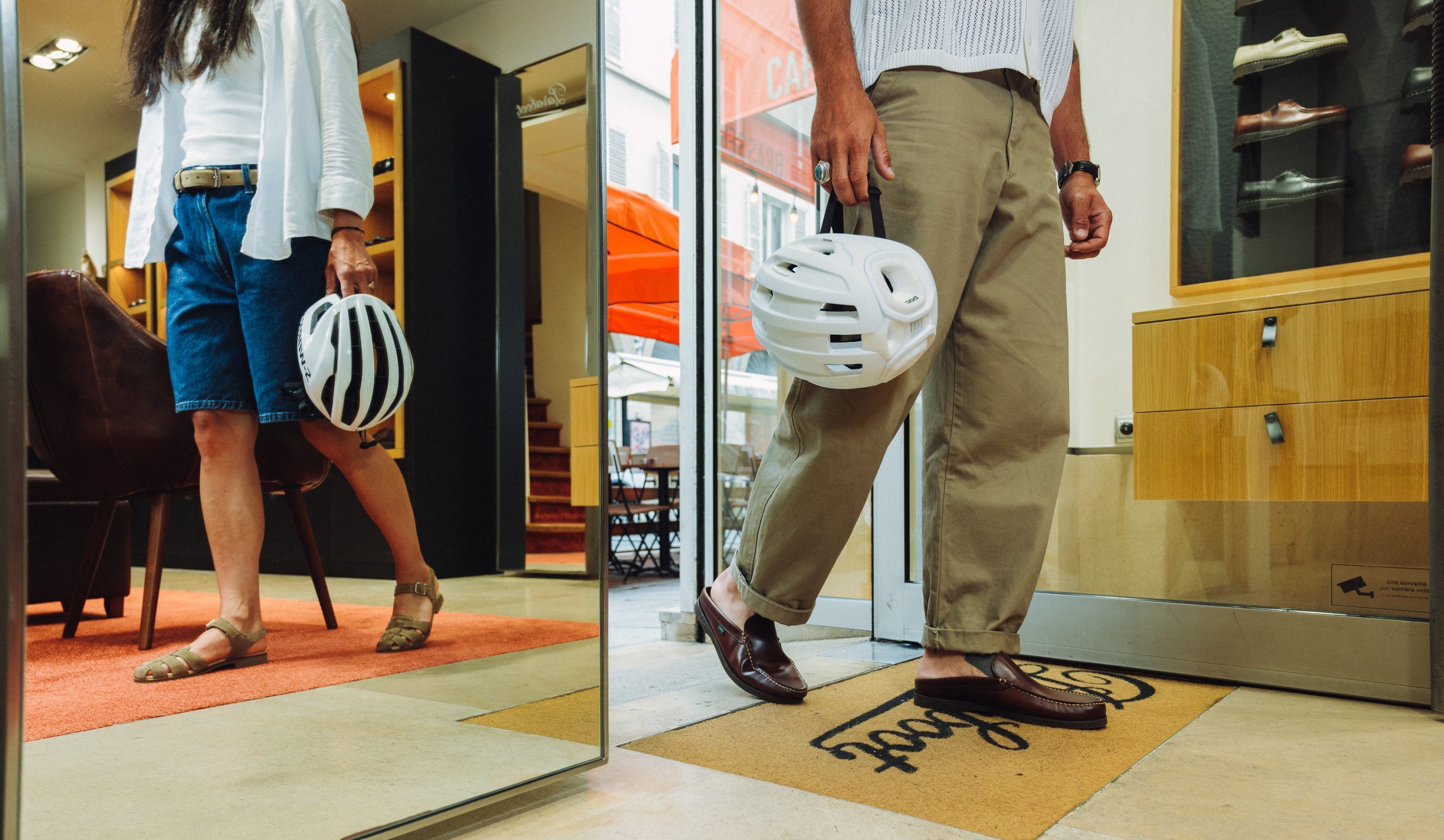 Homme et femme sortant d'une boutique Paraboot avec casques de vélo, portant les mules Bahamas et sandales Bilbao.