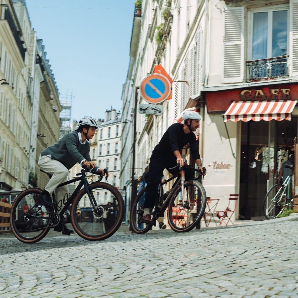 Deux cyclistes grimpant une rue pavée à Montmartre chaussés de derbies Paraboot Avignon et Veley.