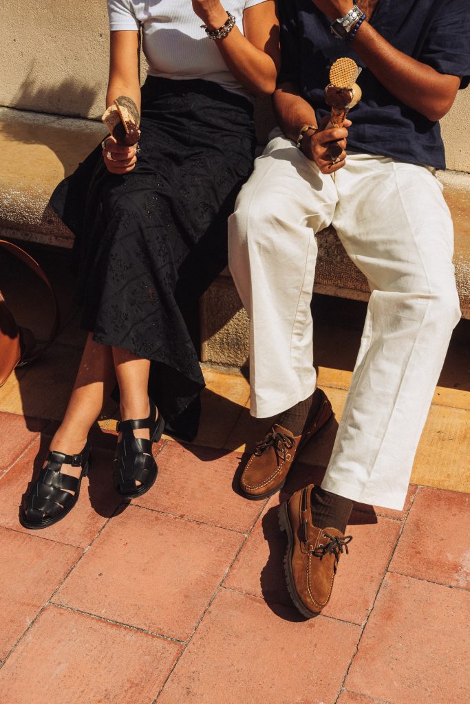 Gros plan sur des chaussures bateau en cuir velours marron et sandales tressées noires Paraboot portées en été.