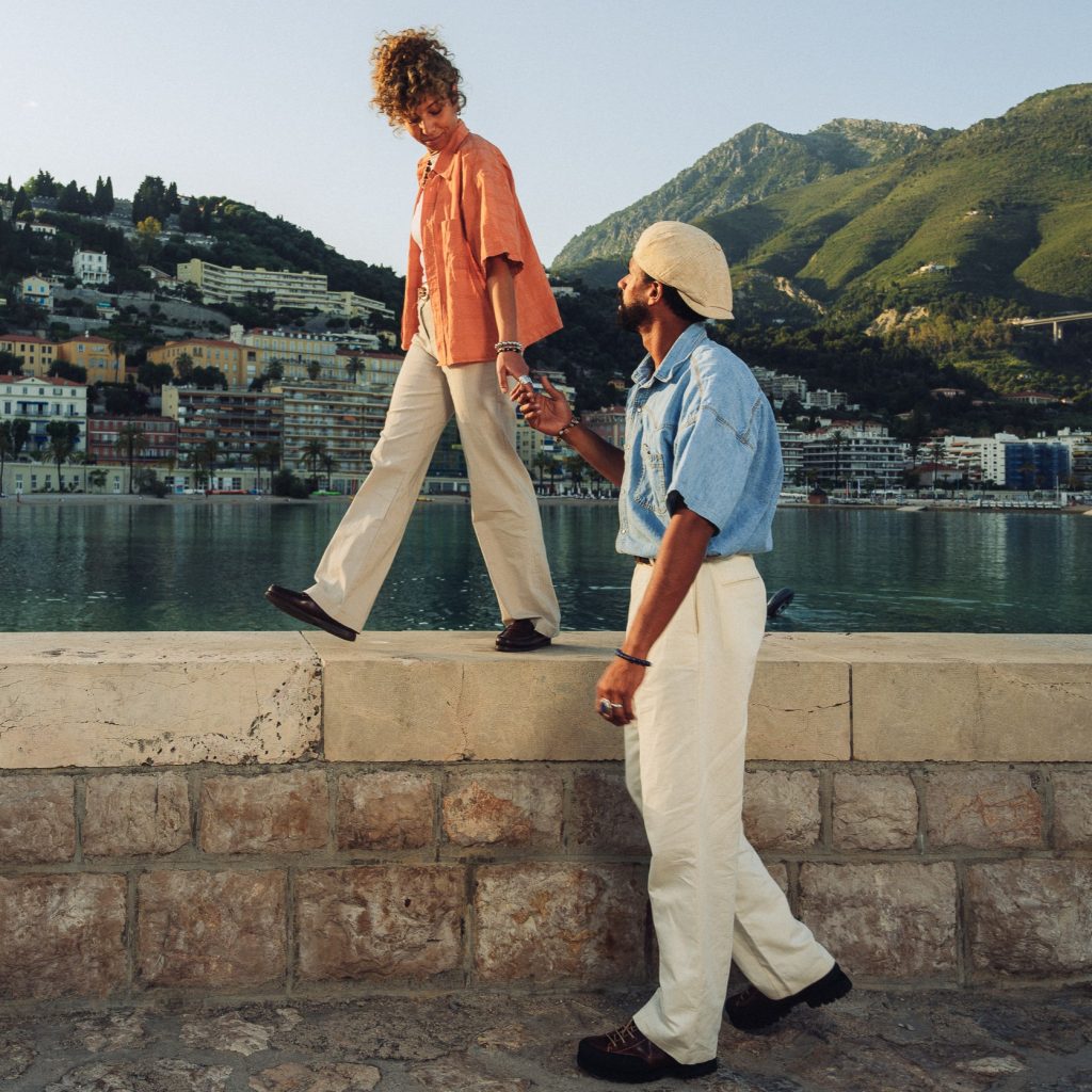 Couple se promenant sur un muret en bord de mer à Menton en chaussures d'été Paraboot. Escapade complice sur le littoral de Menton.