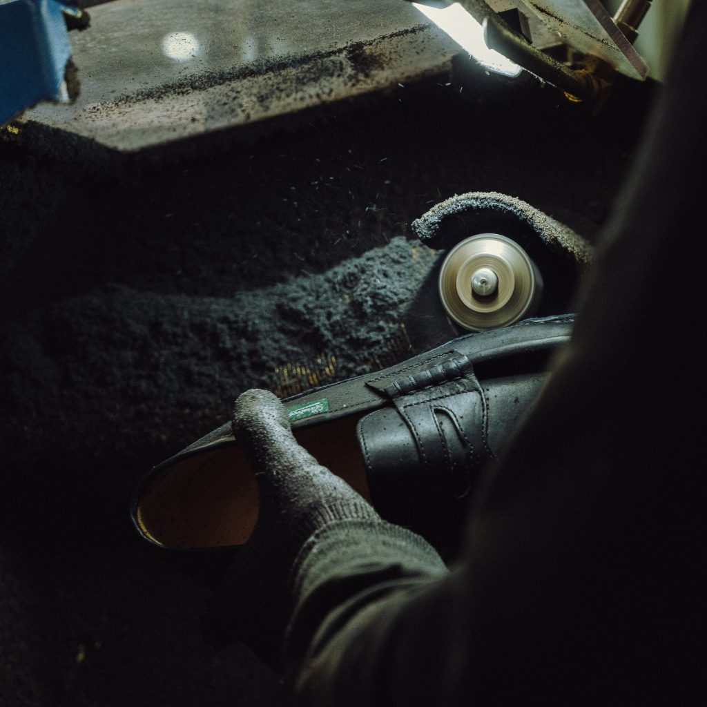 Artisan réalisant le fraisage des bords d'une semelle en gomme sur un mocassin Paraboot Reims en atelier.