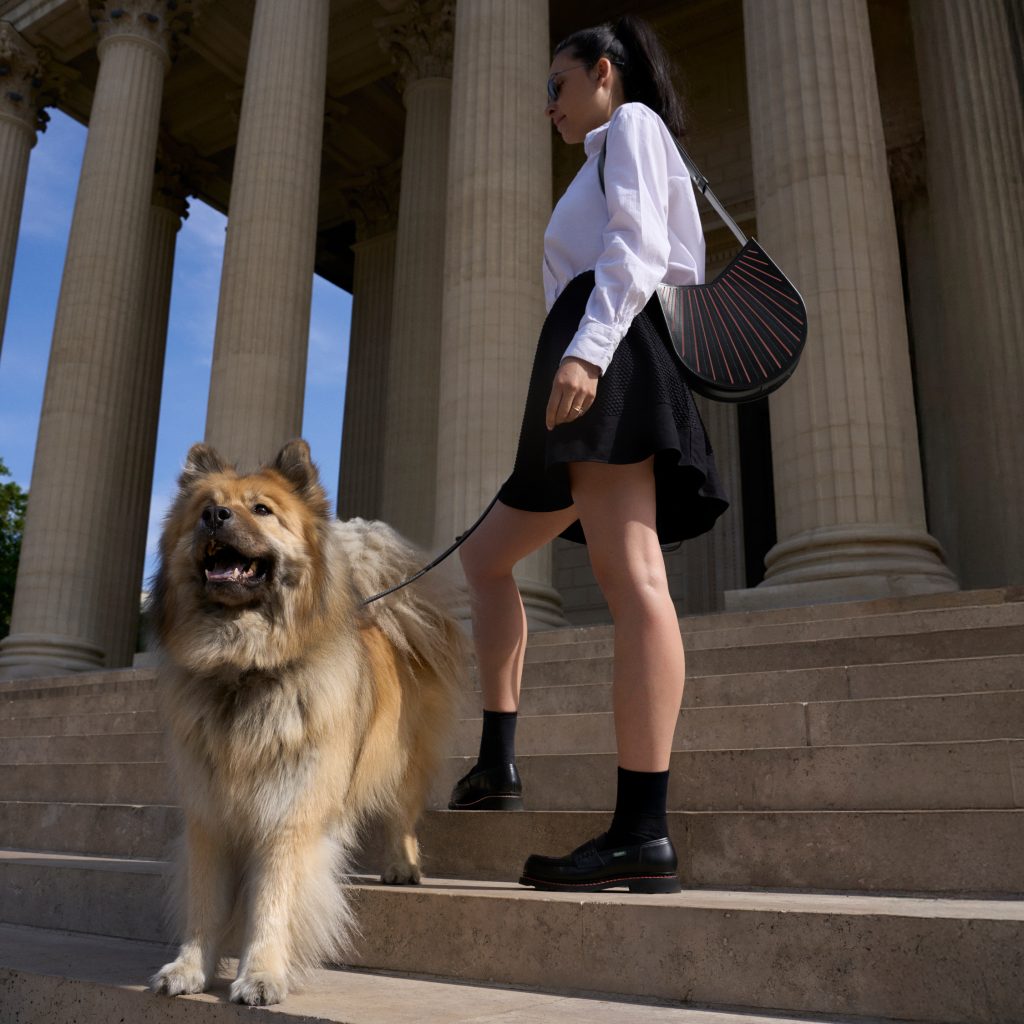 Femme portant le sac Balancier MM et les mocassins Orsay de la collaboration Paraboot x Camille Fournet, promenant son chien sur des marches monumentales.
